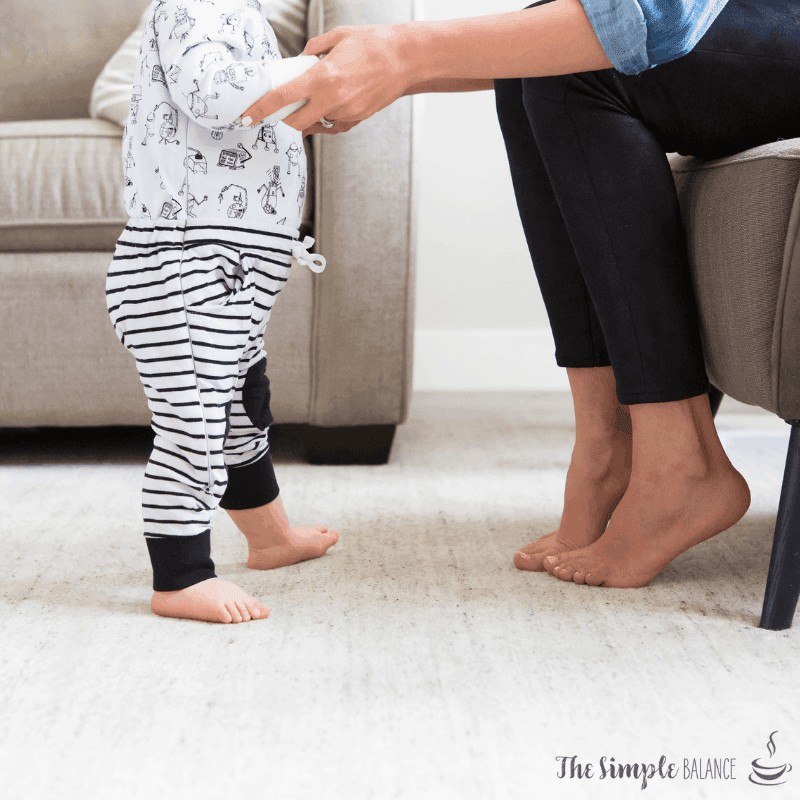 Toddler takes first steps with adult support in a cozy, heartwarming living room scene.
