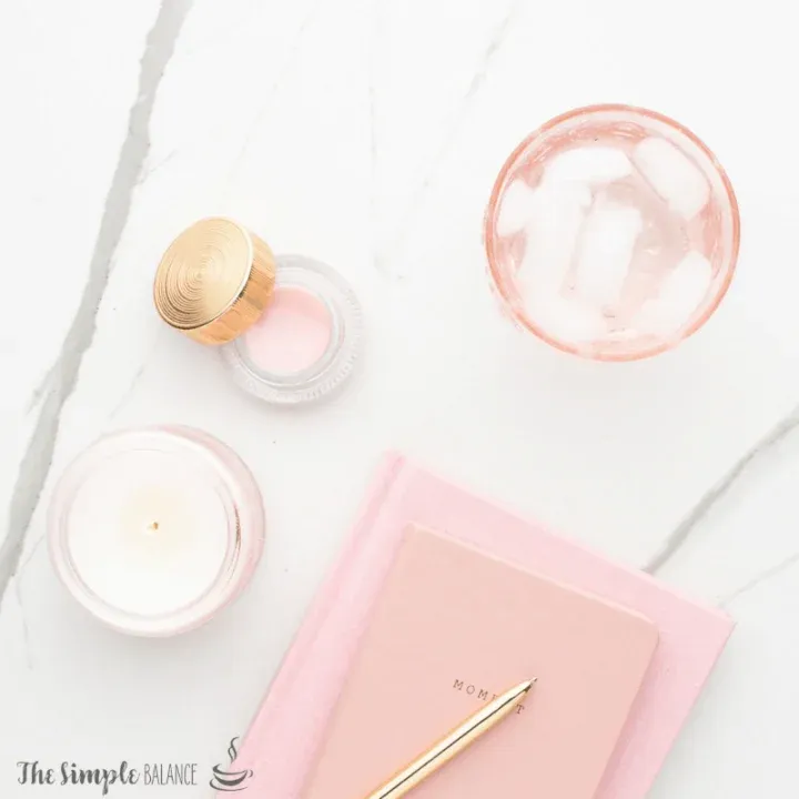 Calming self-care setup with pink candle, MOM notebook, golden pen, and refreshing drink on marble.