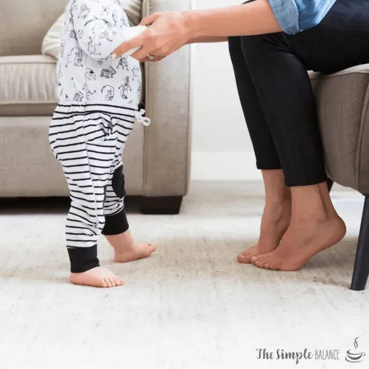 Toddler takes first steps with adult support in a cozy, heartwarming living room scene.